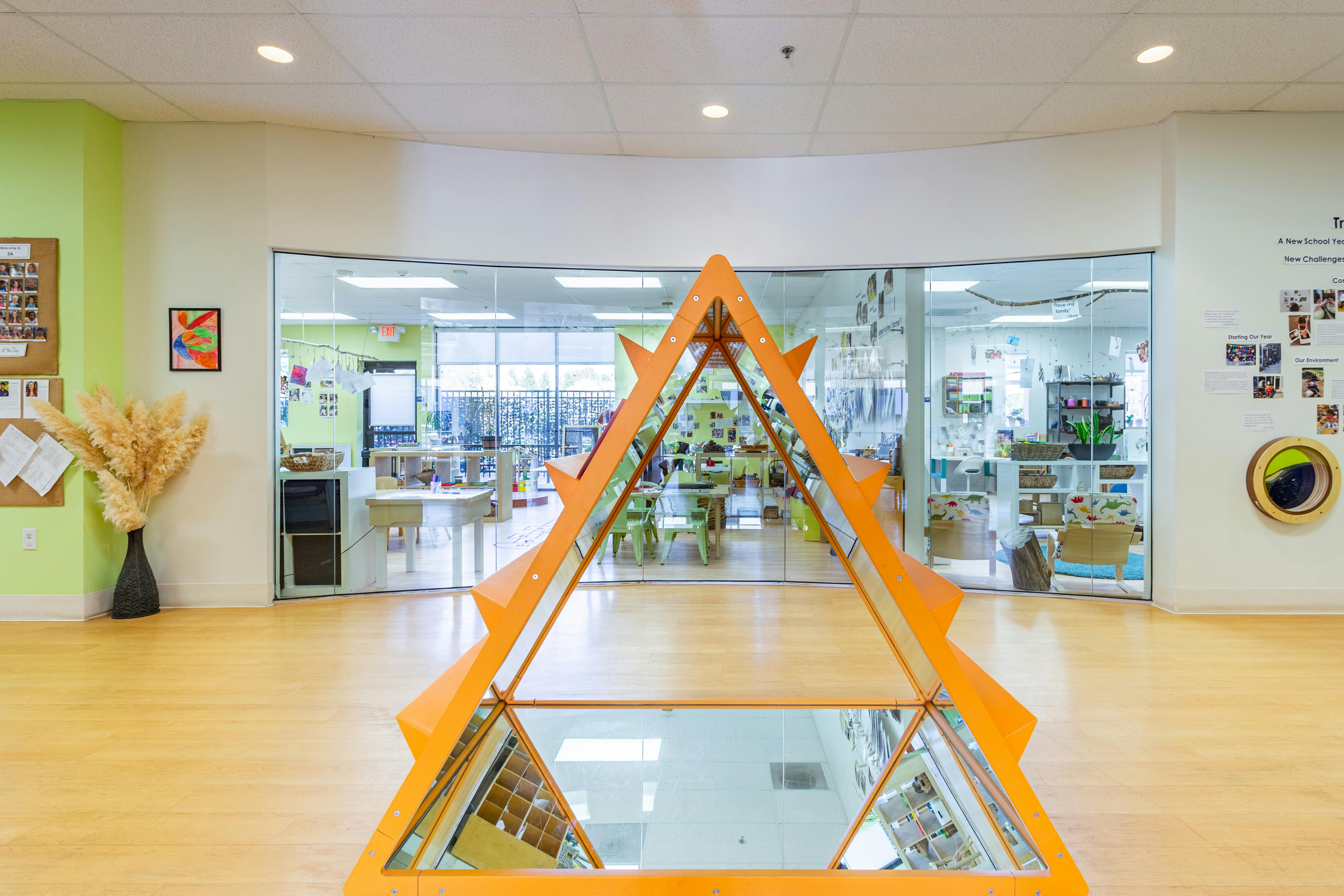 Orange mirrored pyramid sculpture in a hallway with classrooms visible through glass walls
