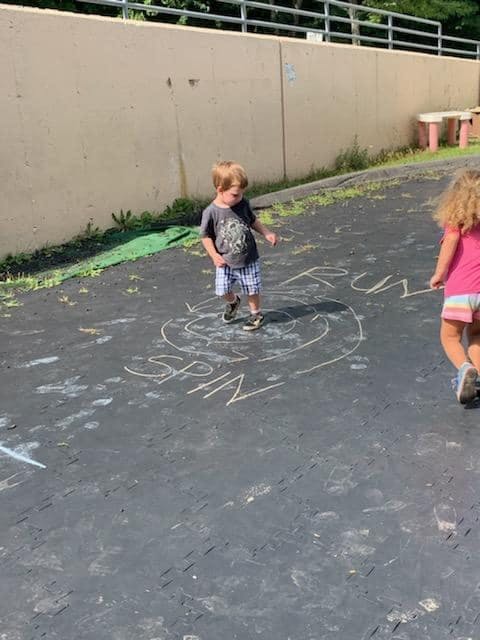 Child standing on chalk drawing with "SPIN" and "RUN" written on pavement