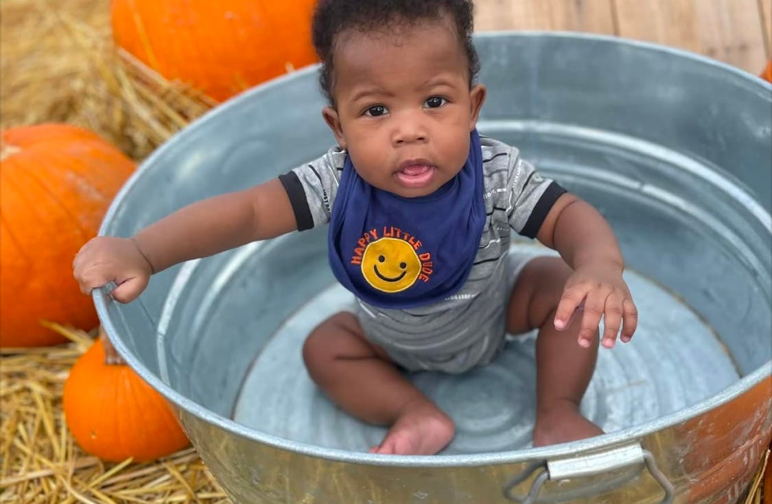 Child in a metal tub with pumpkins and hay around