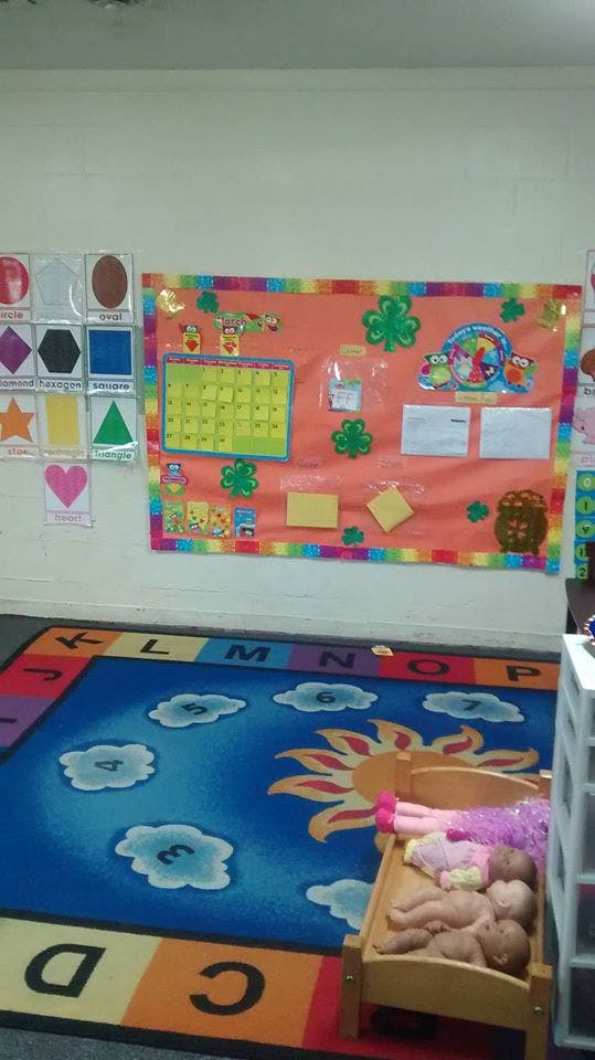 Classroom with a colorful rug, bulletin board, and baby dolls in a crib