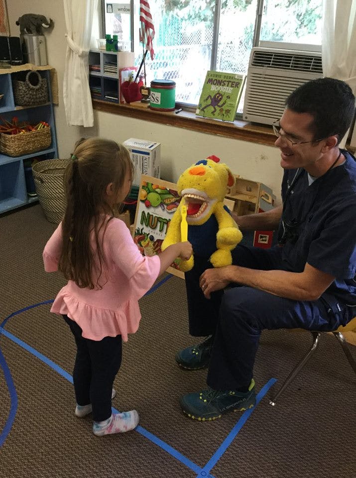 Child brushing teeth of a large yellow stuffed animal with a person