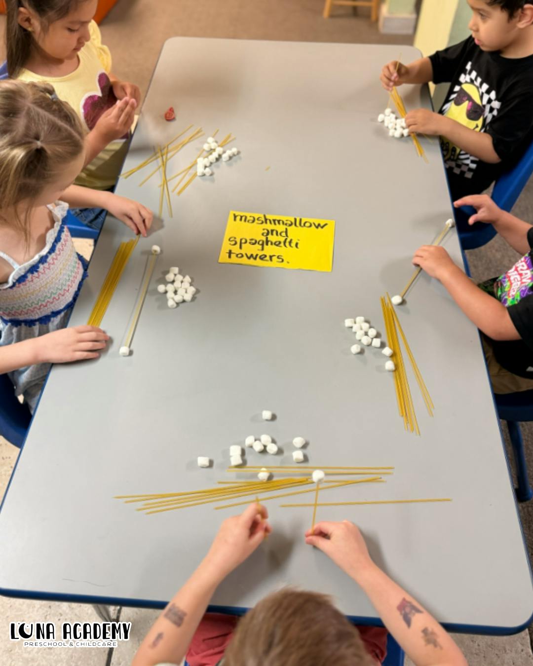 Children building towers with spaghetti and marshmallows at a table