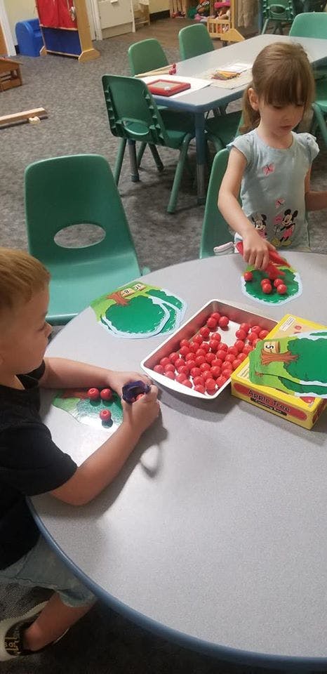 Two children playing with red beads and green tree cutouts at a table