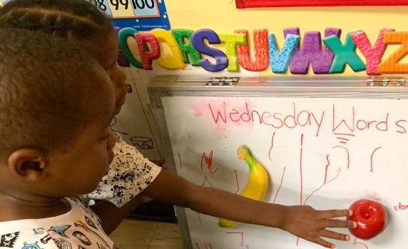 Child reaching for a red apple magnet on a whiteboard