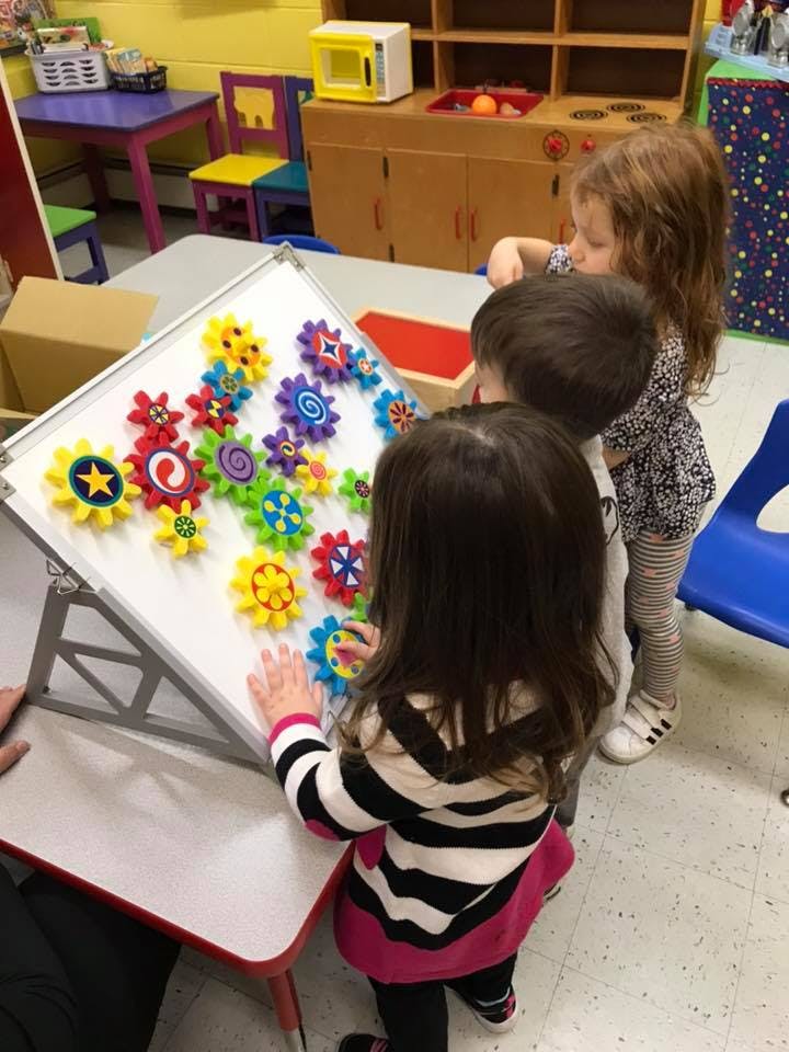Three children playing with colorful gears on a white board in a classroom