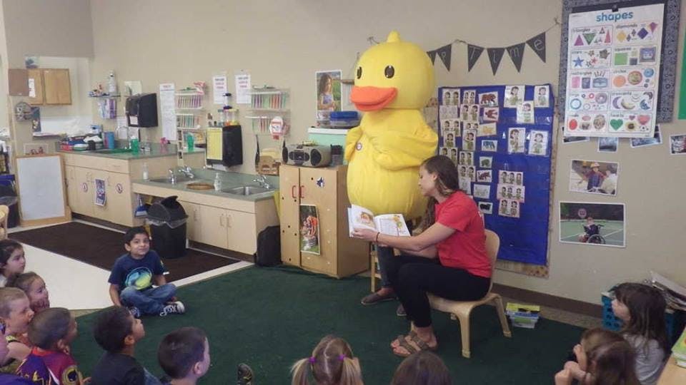 Person in duck costume and person reading to children in a classroom
