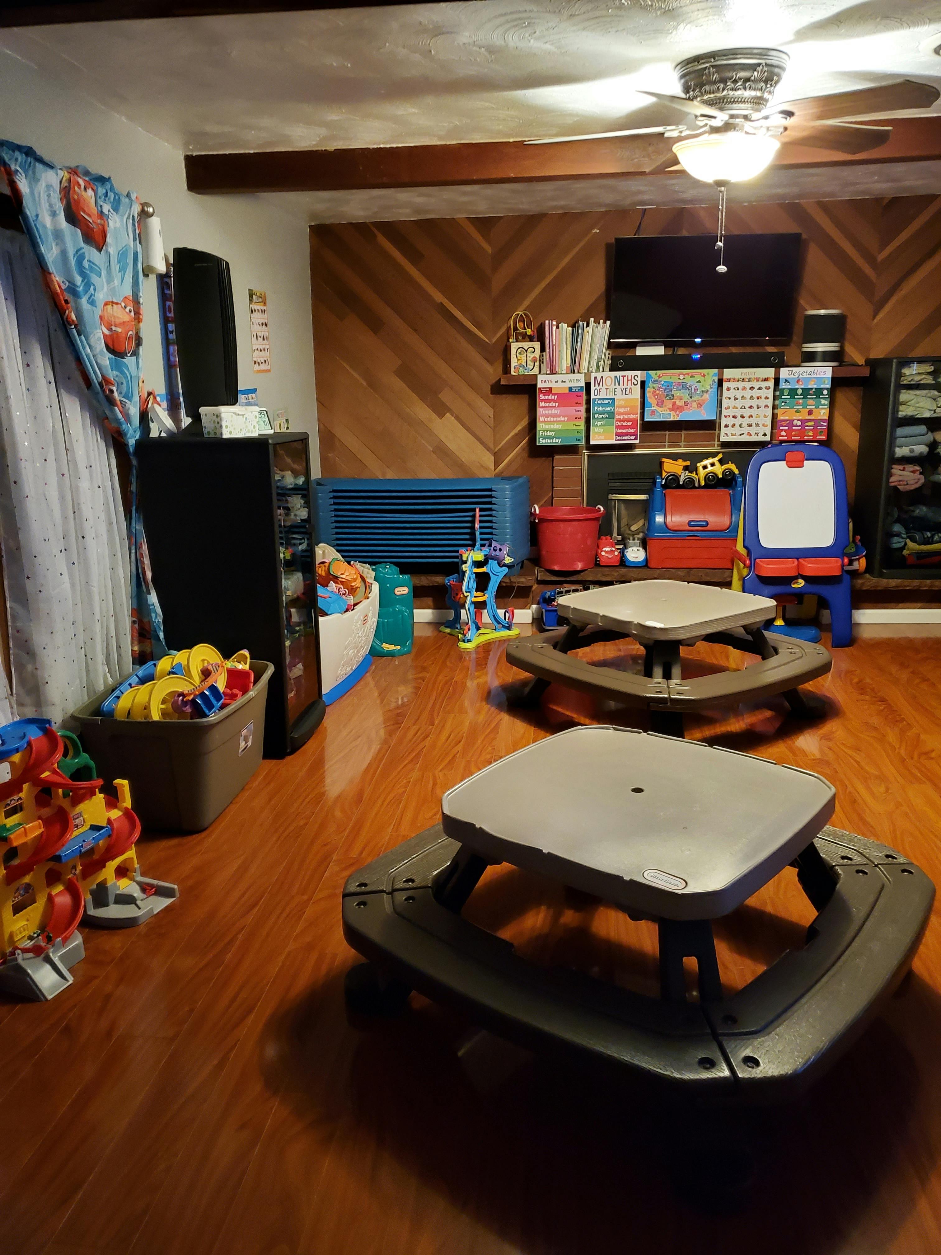 Two small picnic tables on a wooden floor in a room with toys