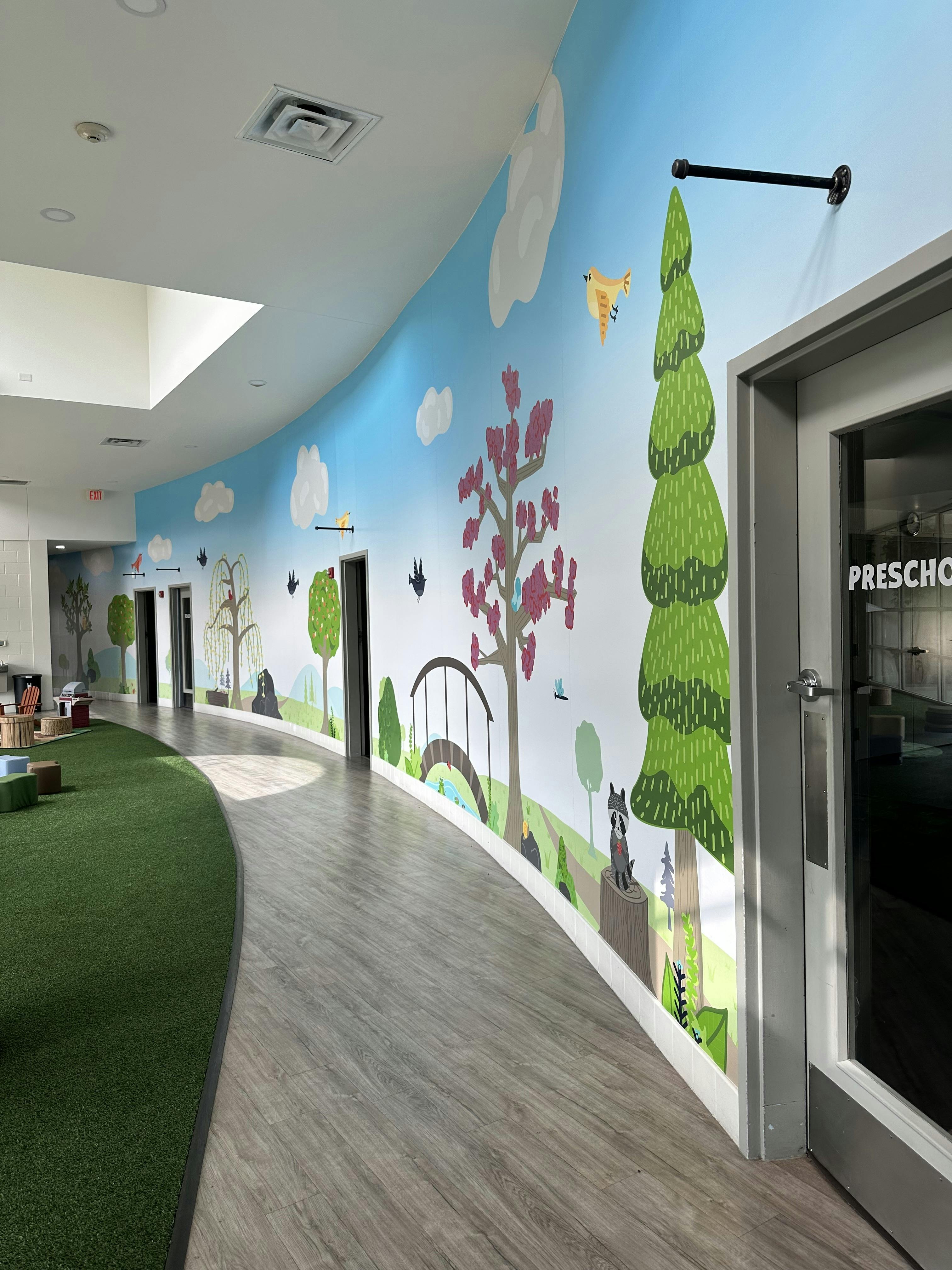 Hallway with a colorful mural of trees and clouds, with a door labeled "PRESCHOOL"