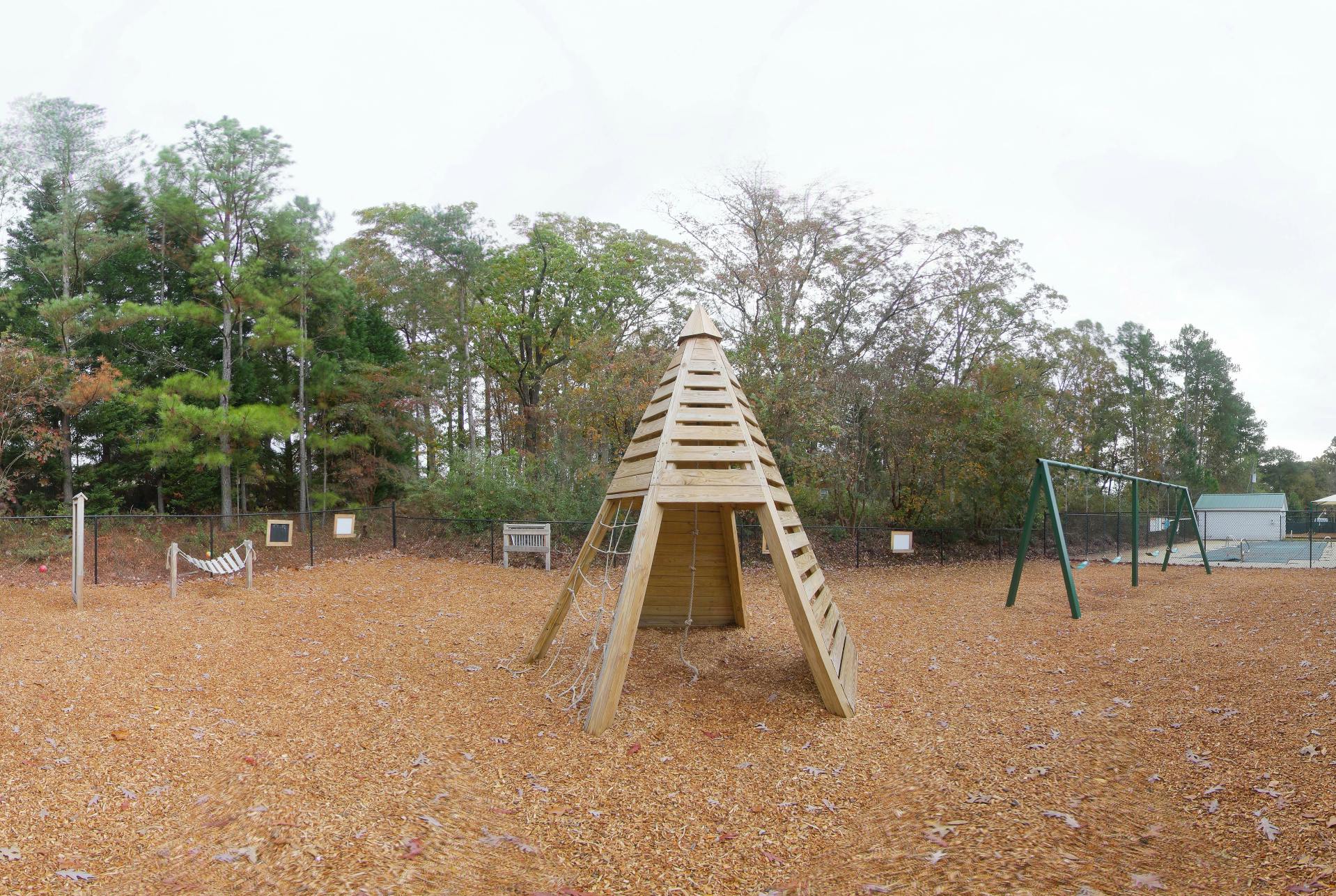 Wooden teepee climbing structure with a swing set and hammock on a playground