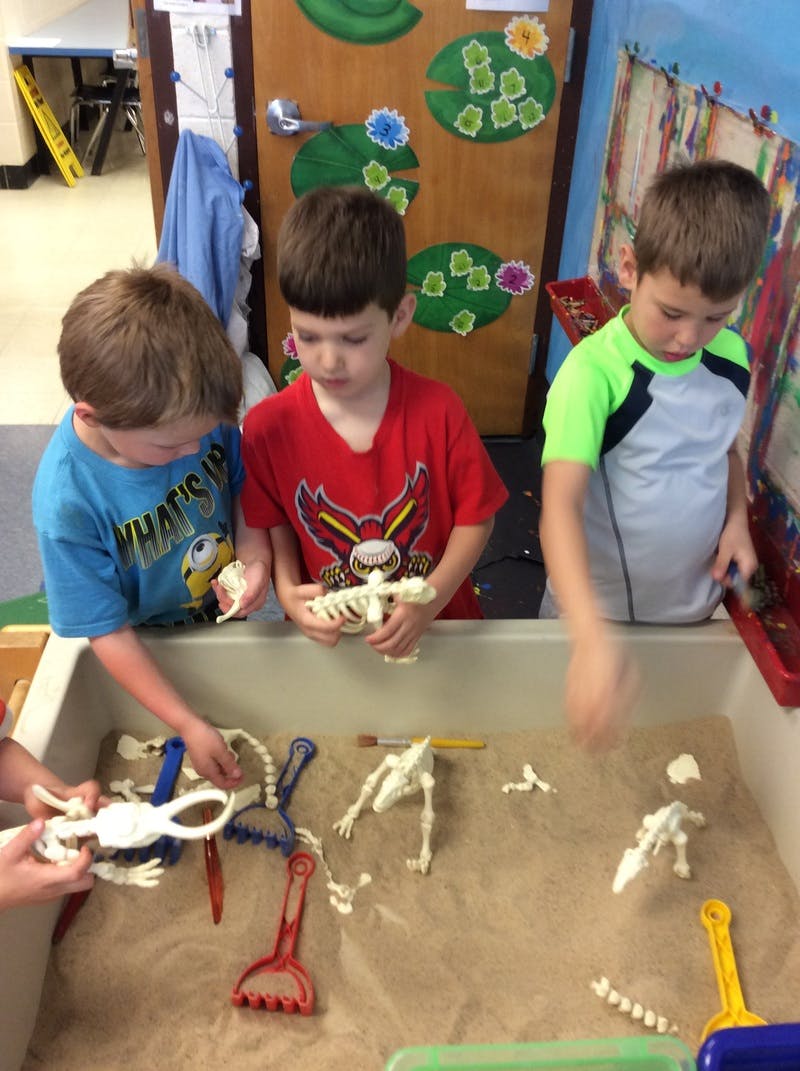 Three children playing with toy skeletons in a sand table
