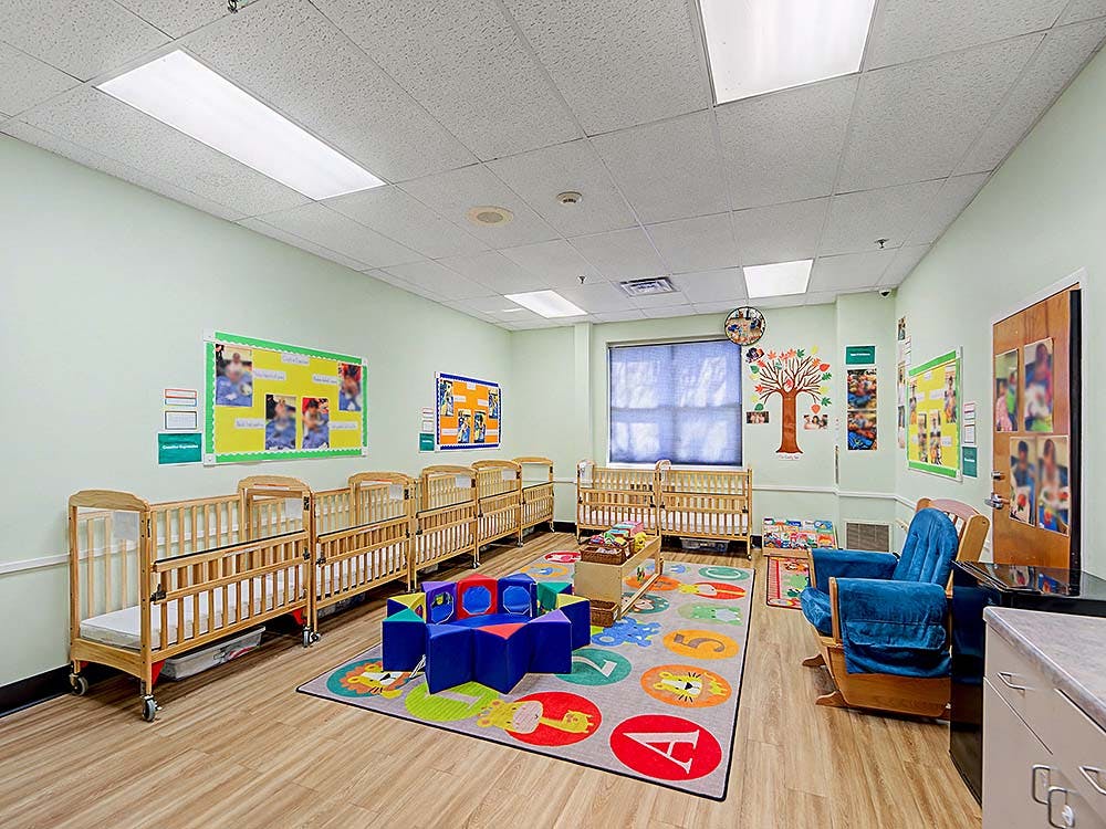 A room with multiple cribs, a colorful rug, and soft play blocks