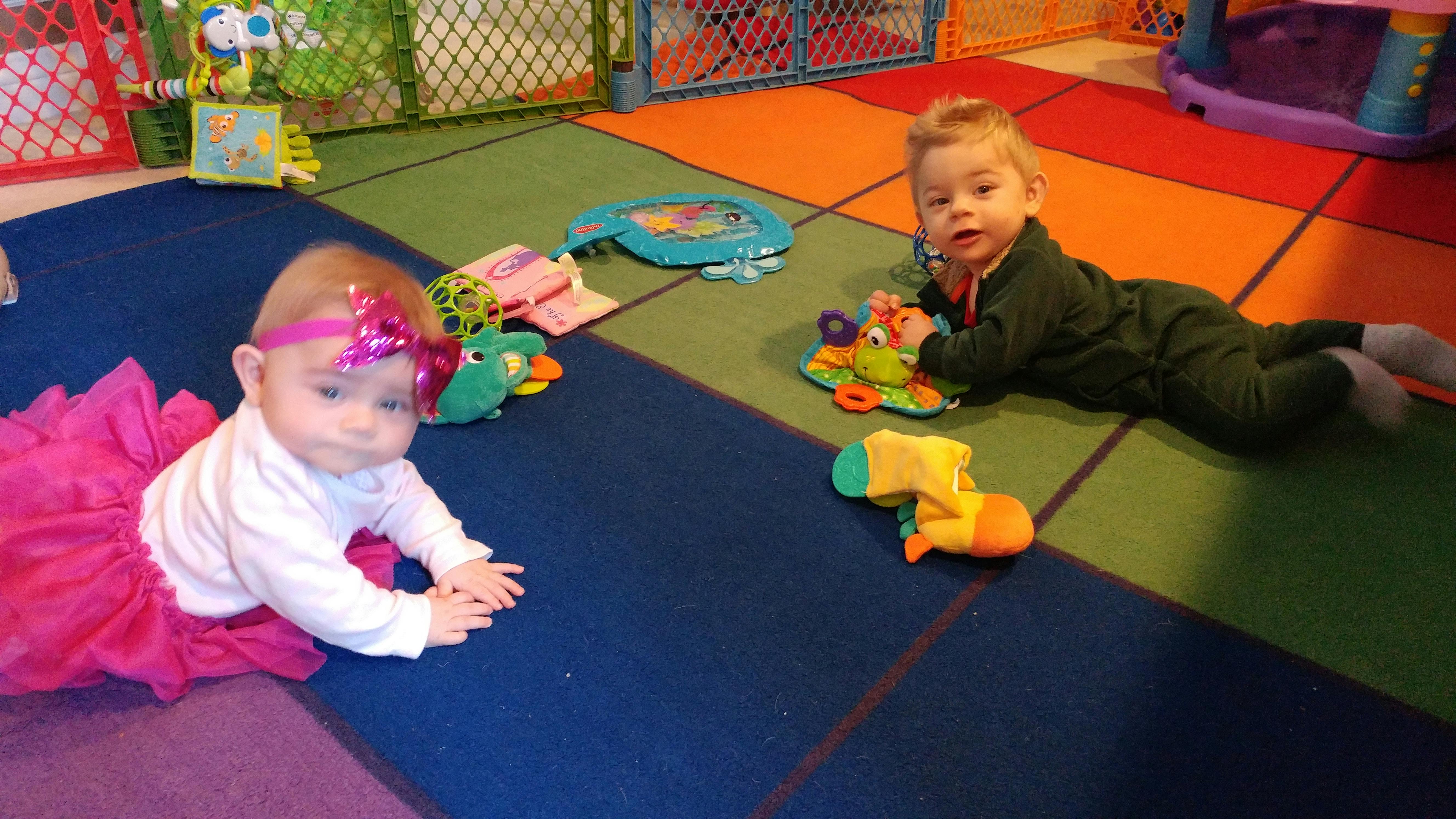 Two infants on a colorful play mat with toys
