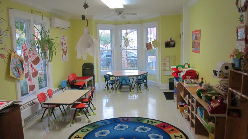 Classroom with small tables and chairs, shelves, and a round rug