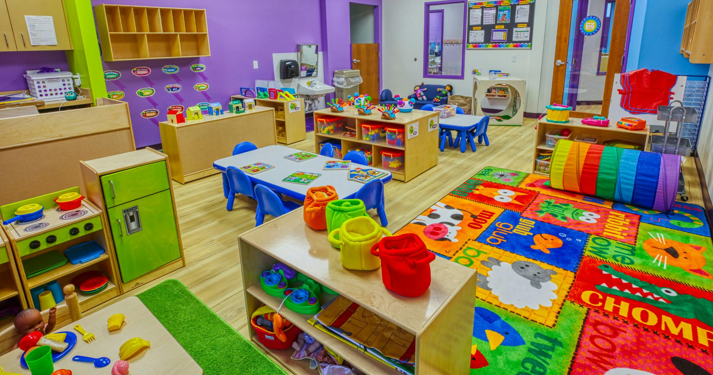 Colorful playroom with small tables, chairs, toys, and a rainbow play tunnel