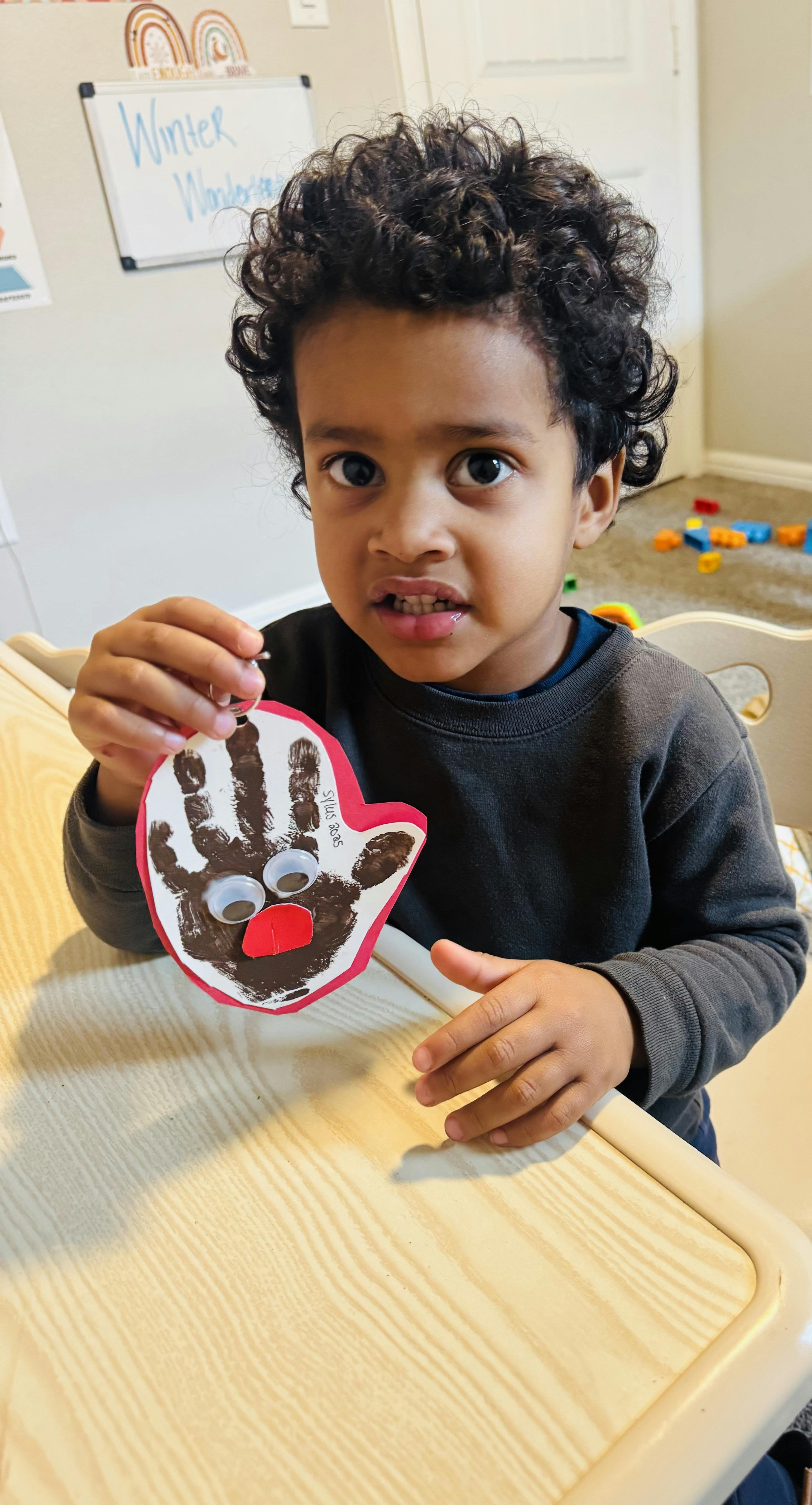Child holding a handprint craft with googly eyes and a red nose