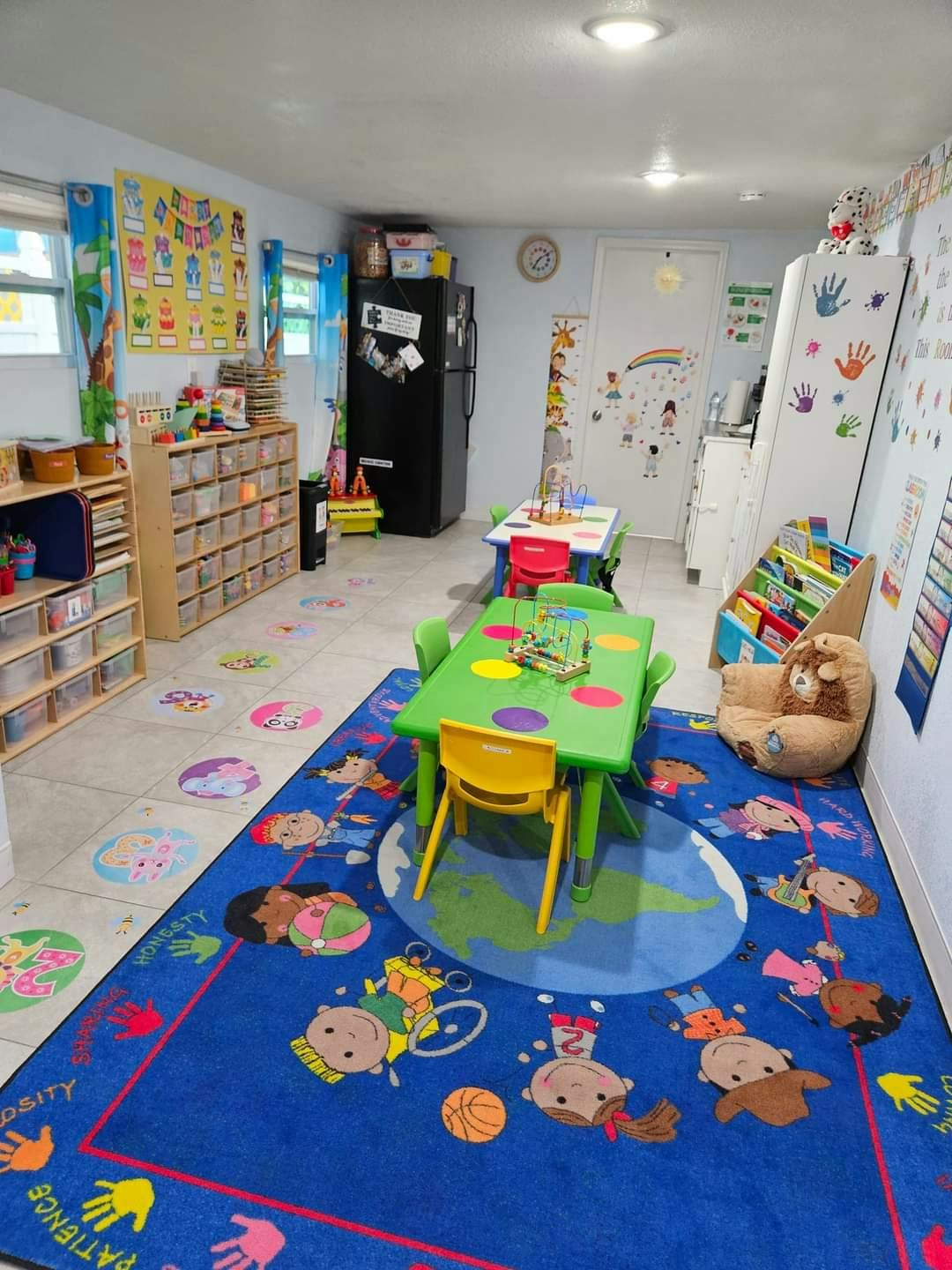 Classroom with small tables and chairs, storage shelves, and a colorful rug