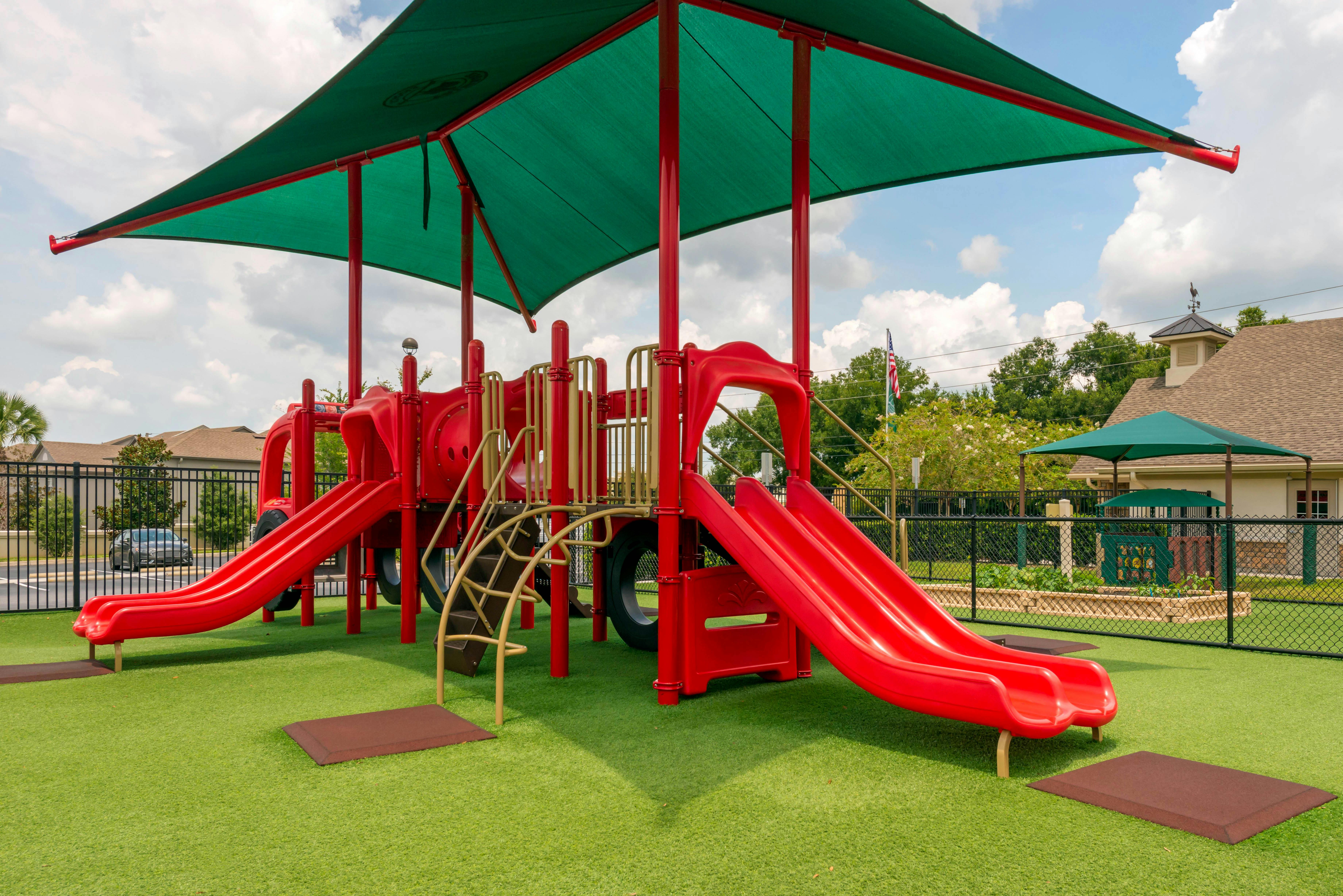 A red and gold playground with multiple slides on artificial green turf