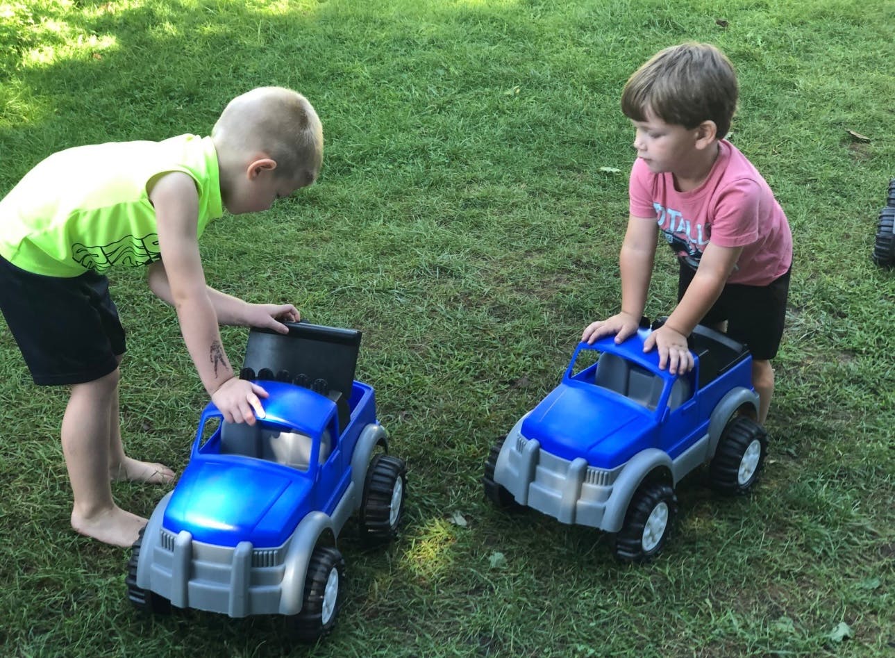 Two children playing with blue toy trucks on grass