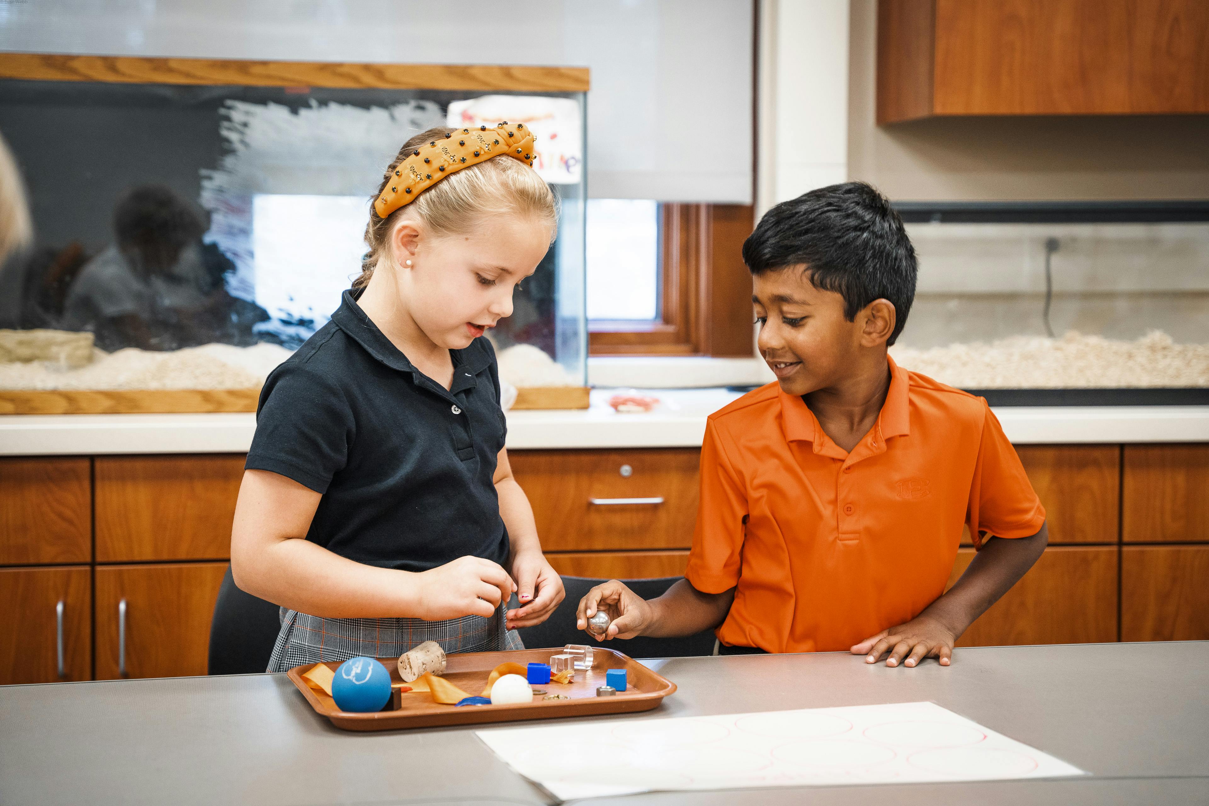Two children working with small objects on a tray in a classroom