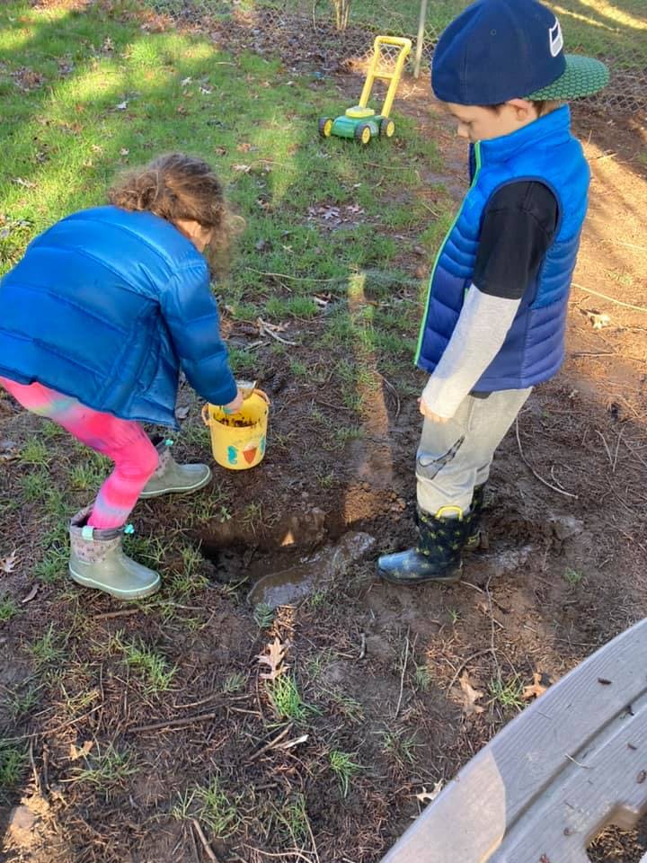 Two children playing in dirt with a bucket