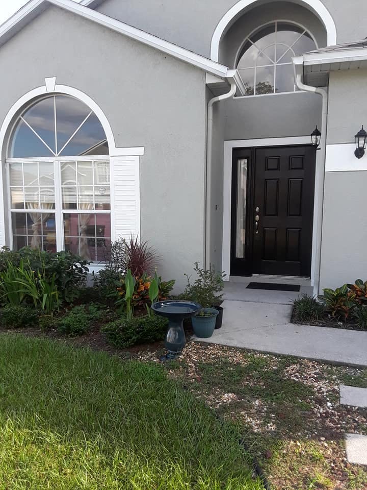 Front exterior of a house with a black door, arched window, and landscaping