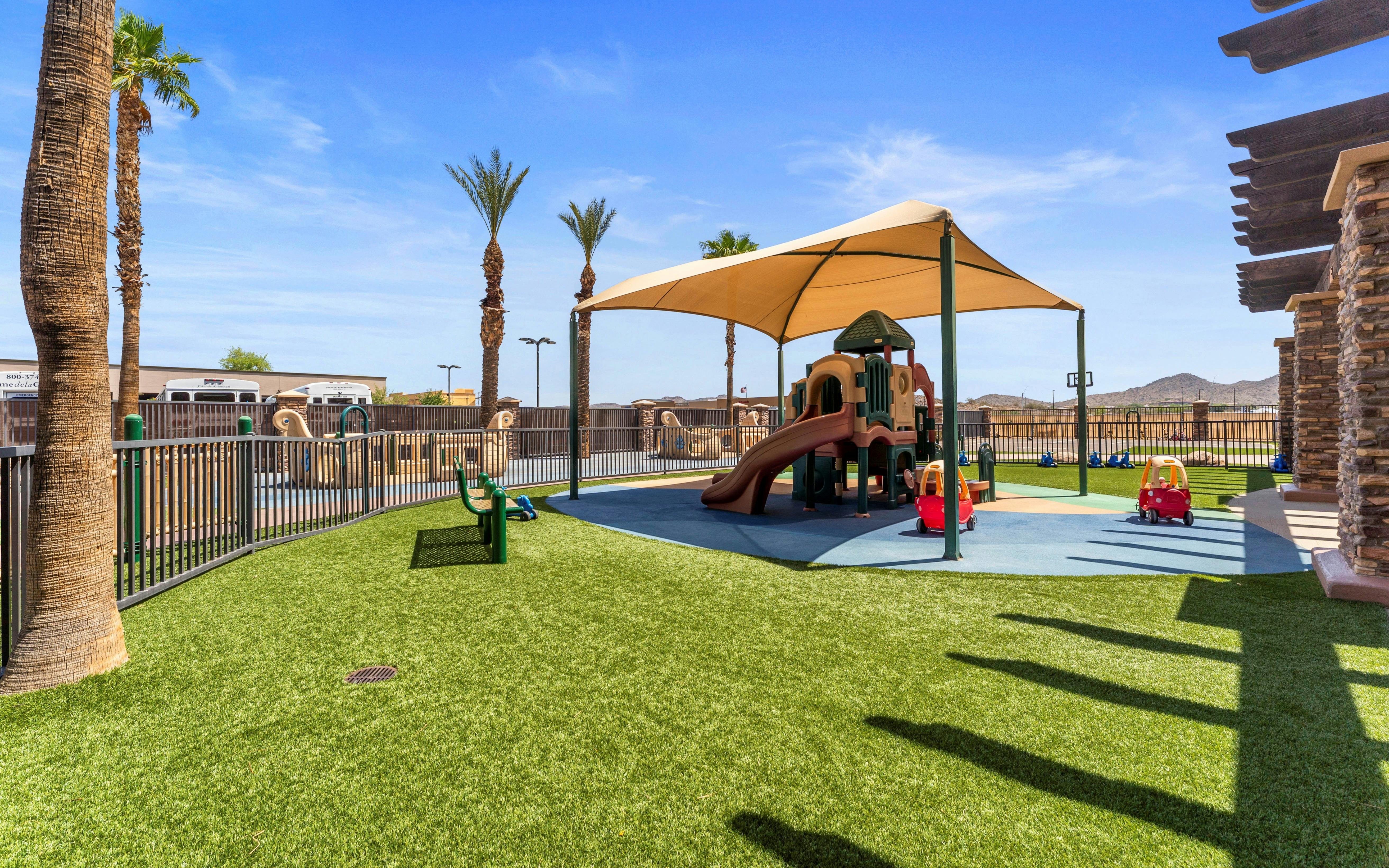 Playground with climbing structure, slide, shaded area, and artificial turf