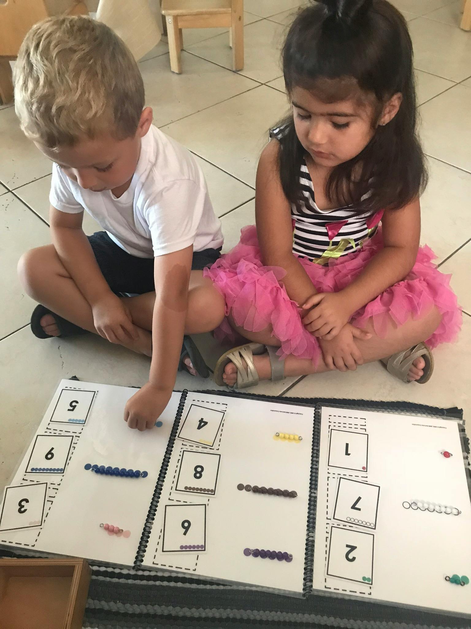 Two children sitting on the floor playing with a number matching game