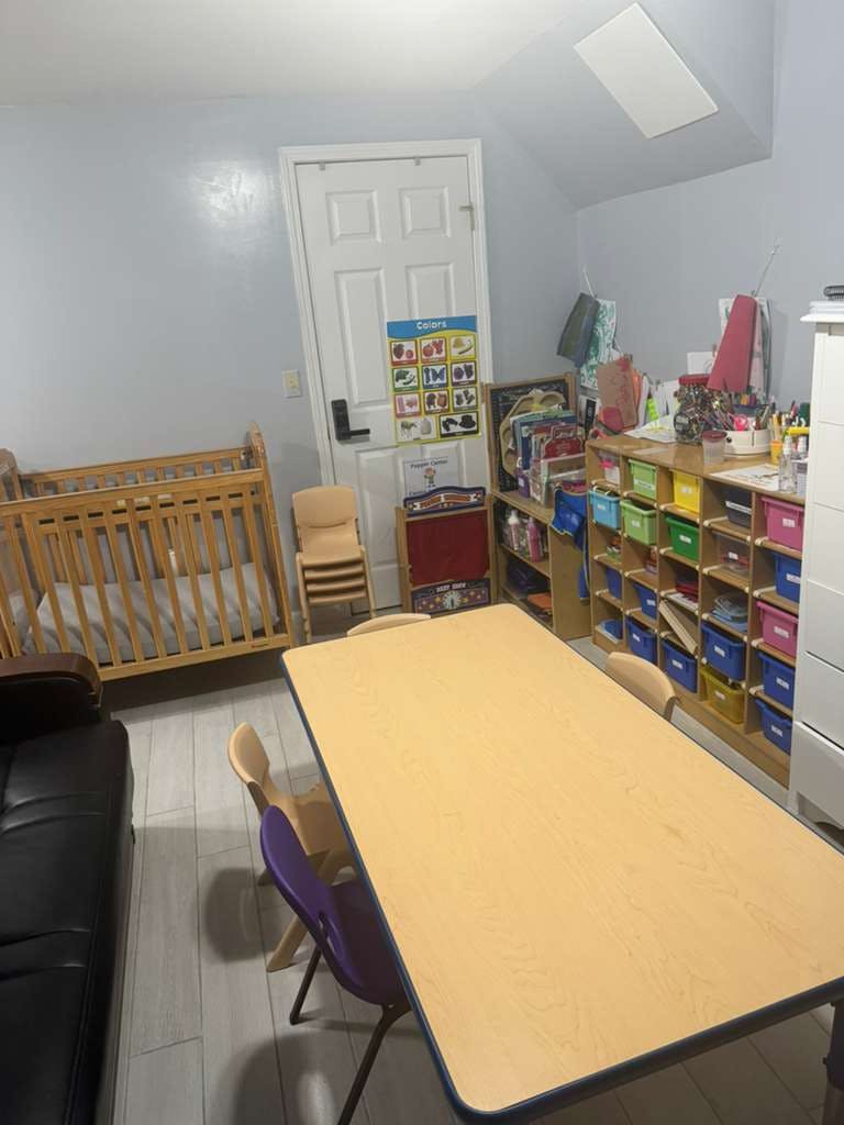 Classroom interior with small chairs around a table, a crib, and storage bins