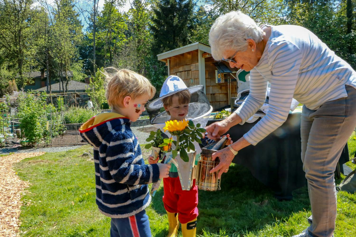 Adult and two children with flowers and a beehive