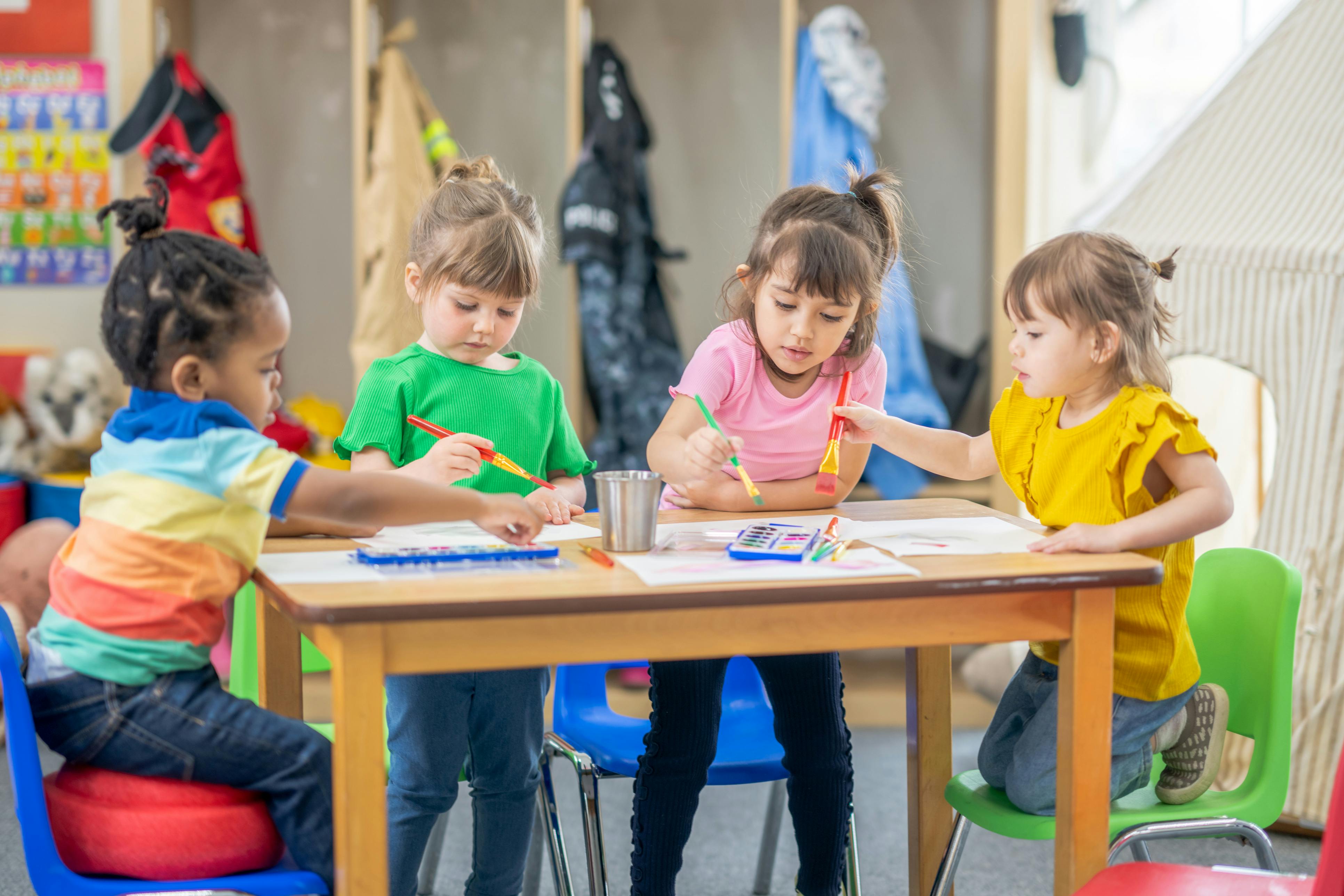 Four children sitting at a table painting in a classroom