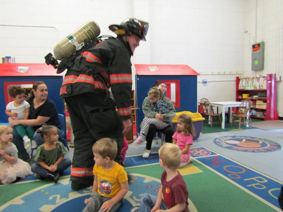 Firefighter in uniform with air tank interacting with children in a classroom