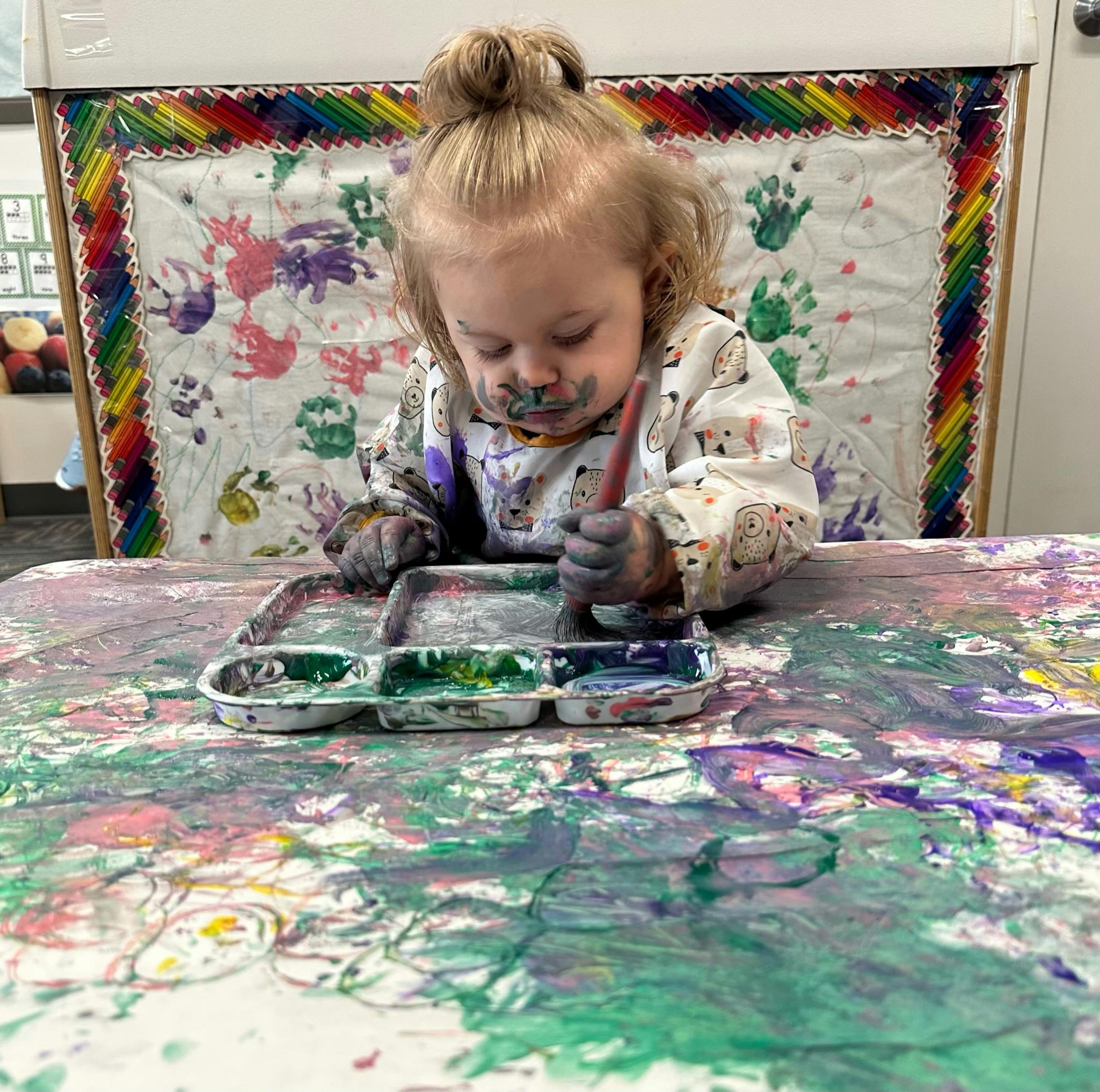 Child painting at a table with a brush and paint palette
