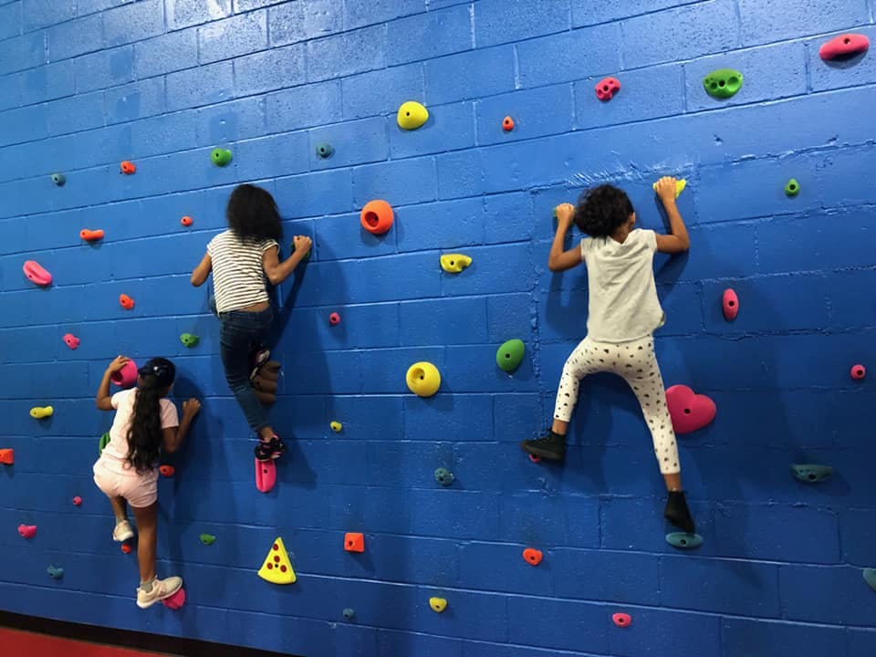 Three children climbing a blue rock wall