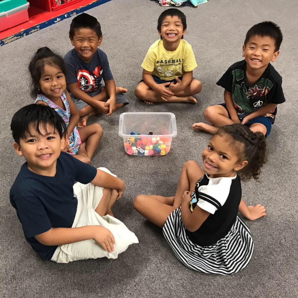 Six children sitting in a circle on the floor around a container of small objects