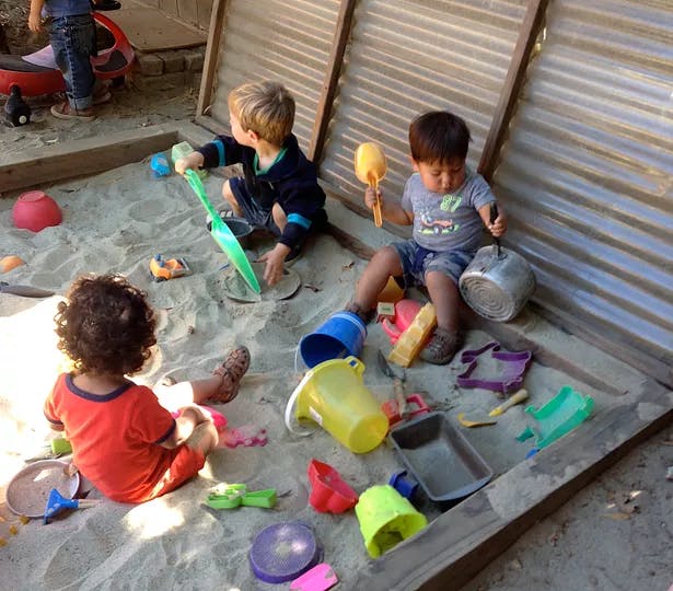 Three children playing in a sandbox with toys