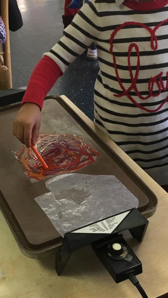 Child using a tool to spread melted crayon wax on paper