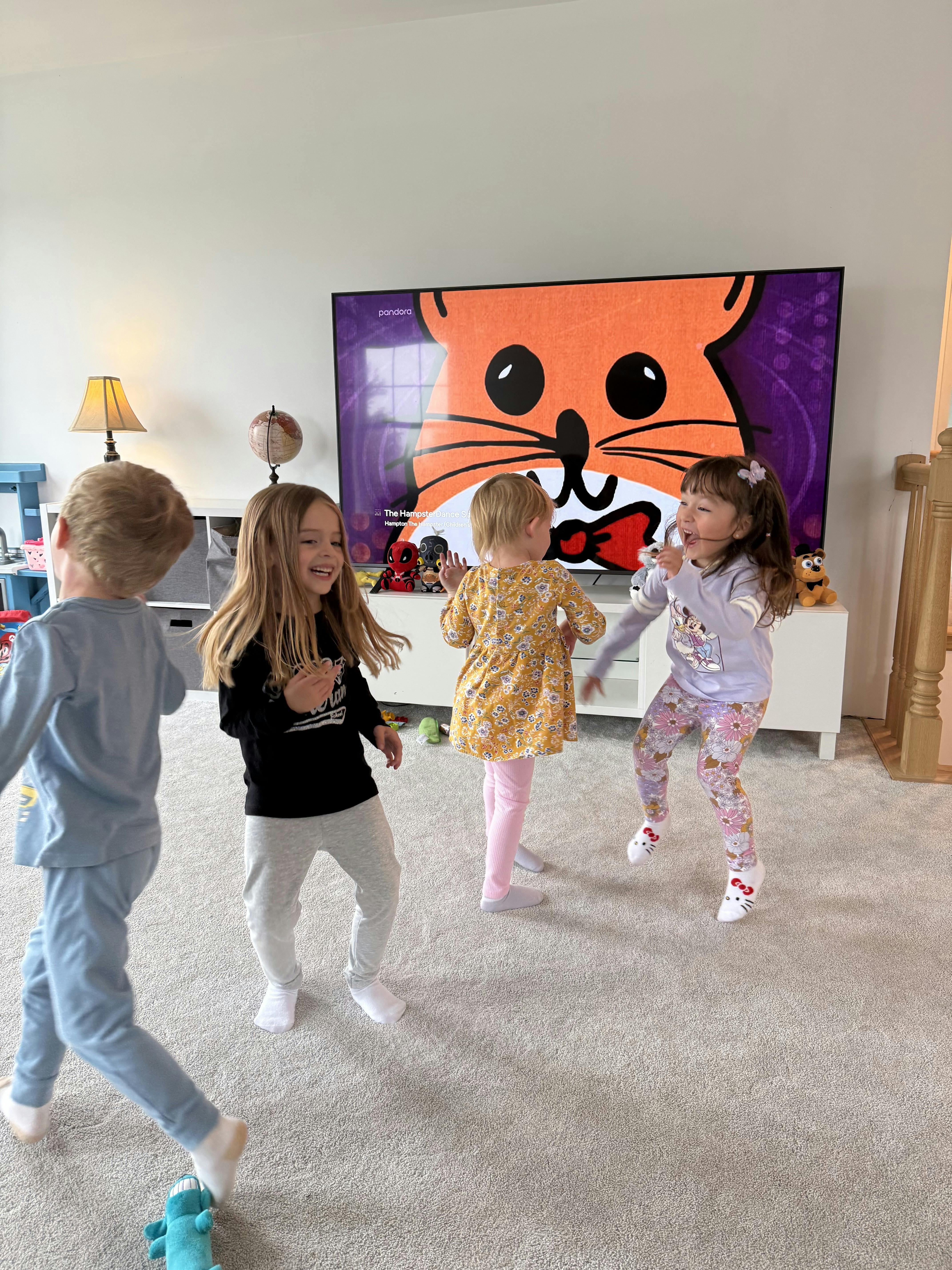 Four children dancing in front of a television screen showing a cartoon character