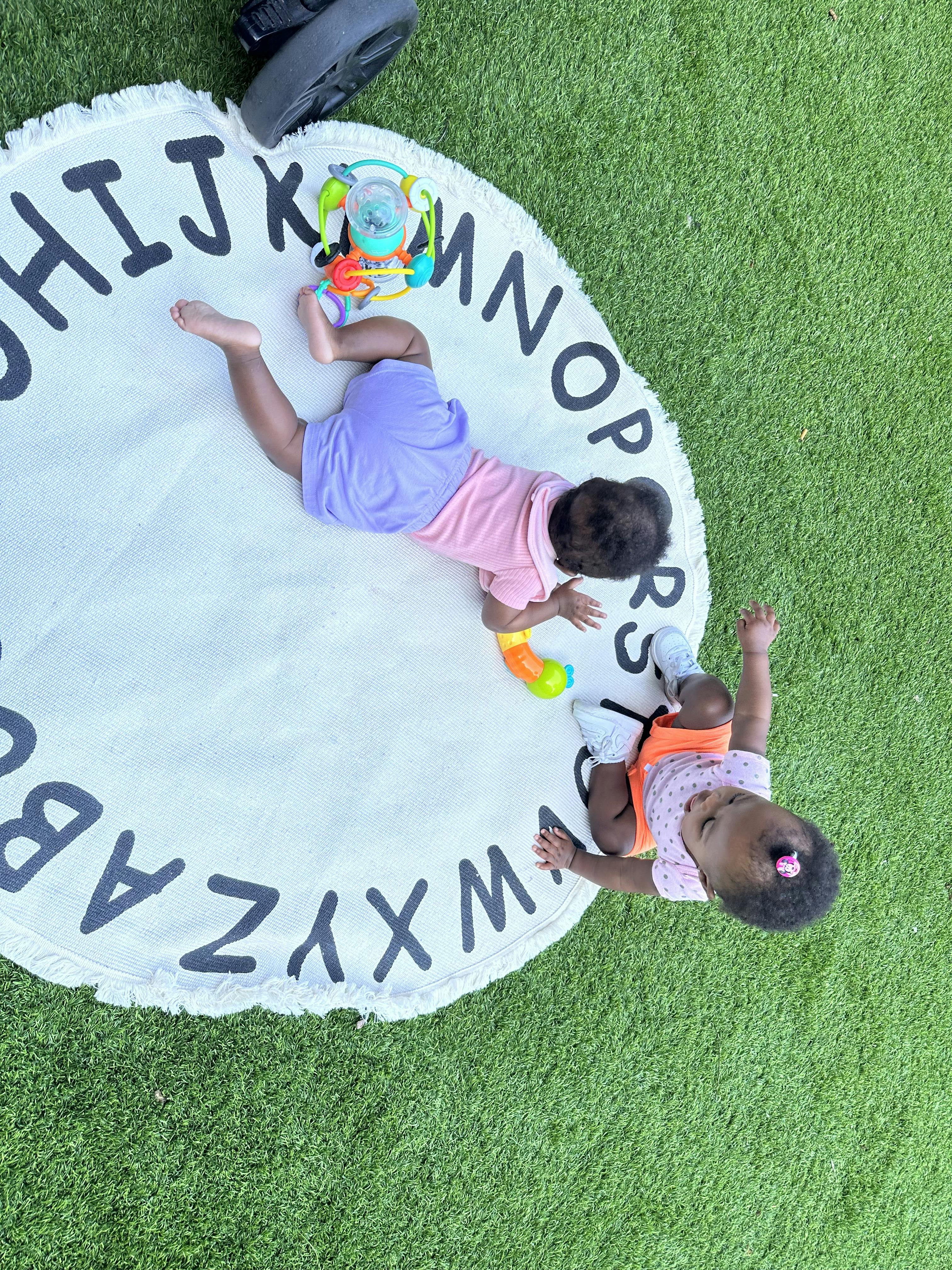 Two children playing on an alphabet mat on grass