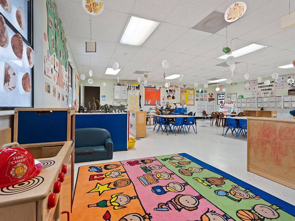 Colorful preschool classroom with tables, chairs, and a play kitchen