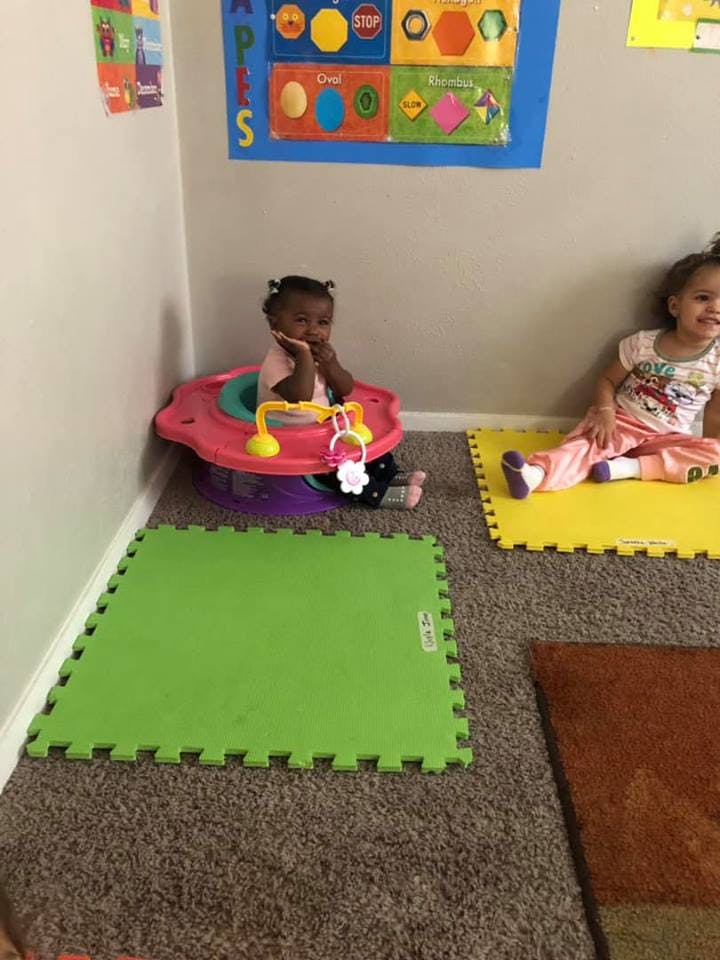 Two children sitting on the floor, one in a baby seat