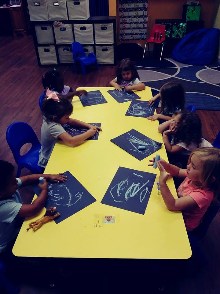 Children drawing on paper at a yellow table