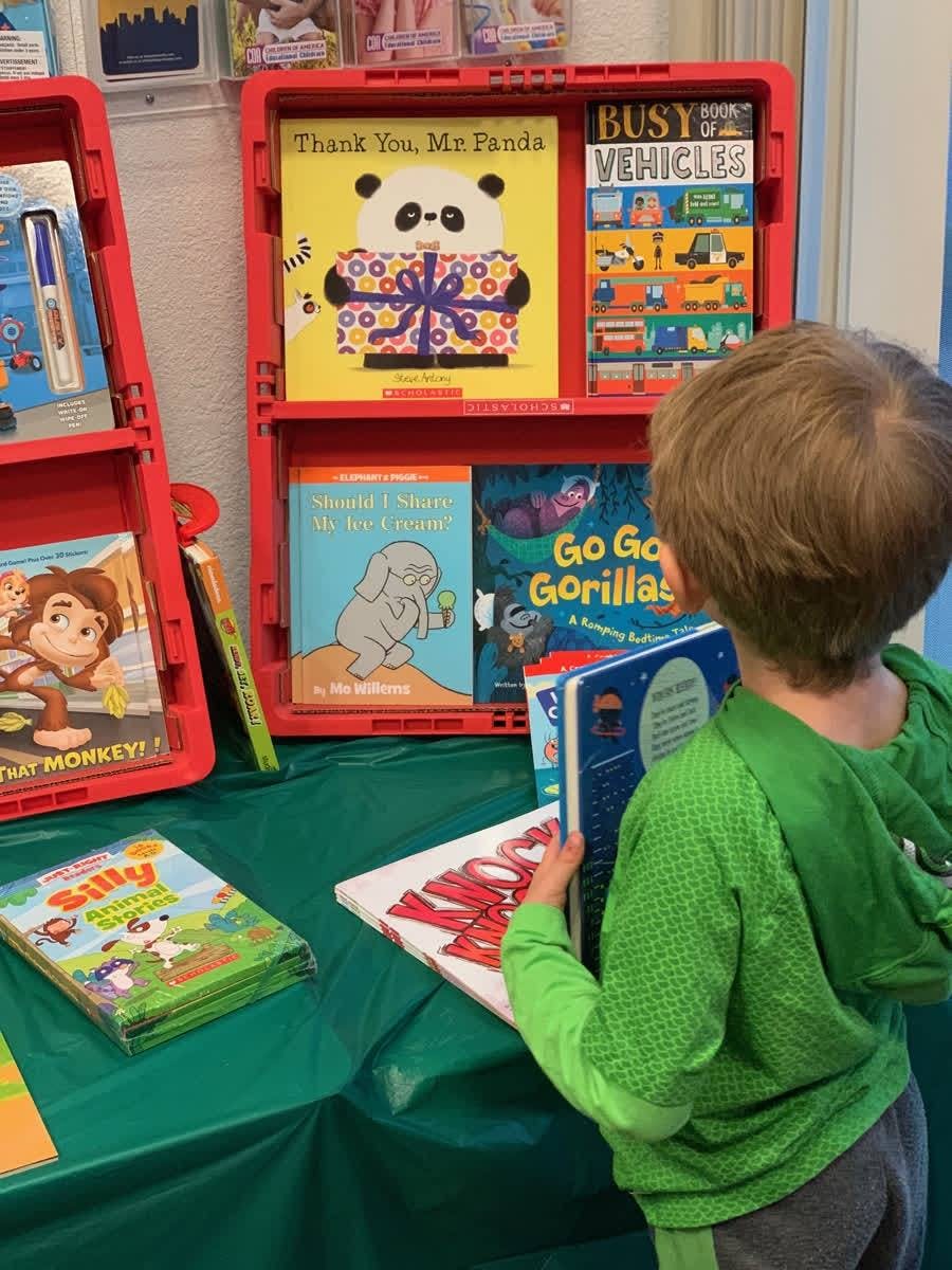 Child looking at books on a table and in a red display shelf