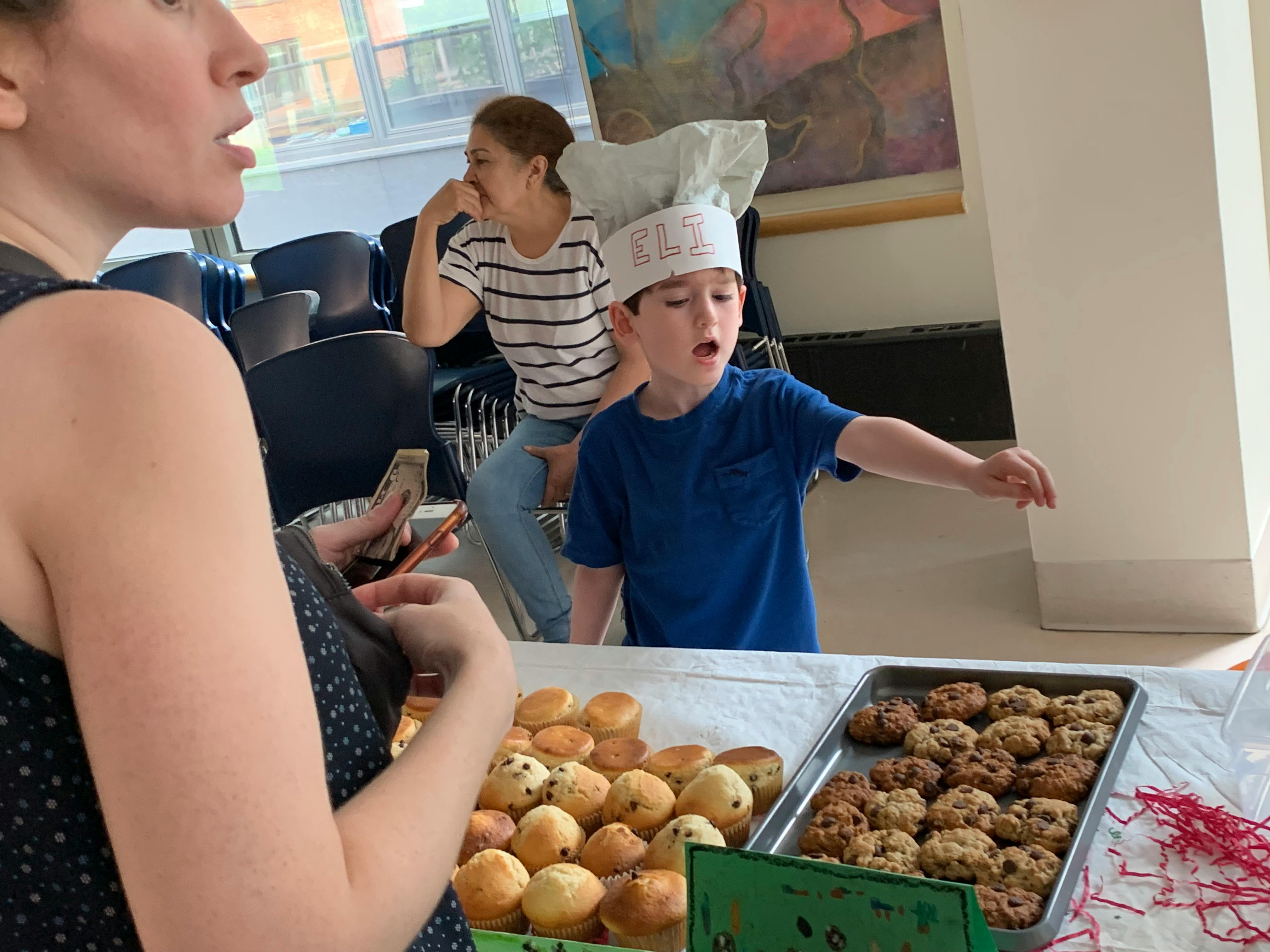 A child in a chef hat with "ELI" written on it, muffins, and cookies