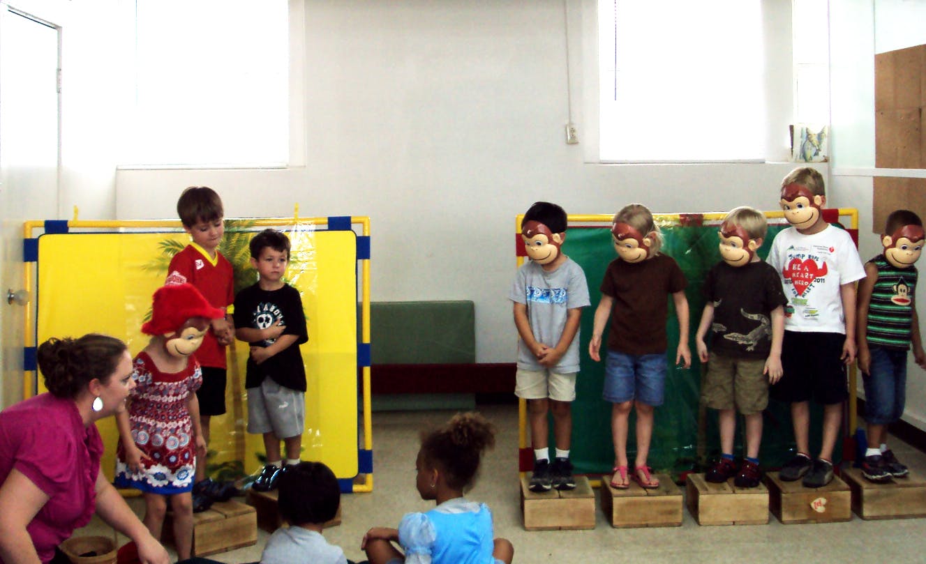 Children wearing monkey masks standing on blocks in a classroom