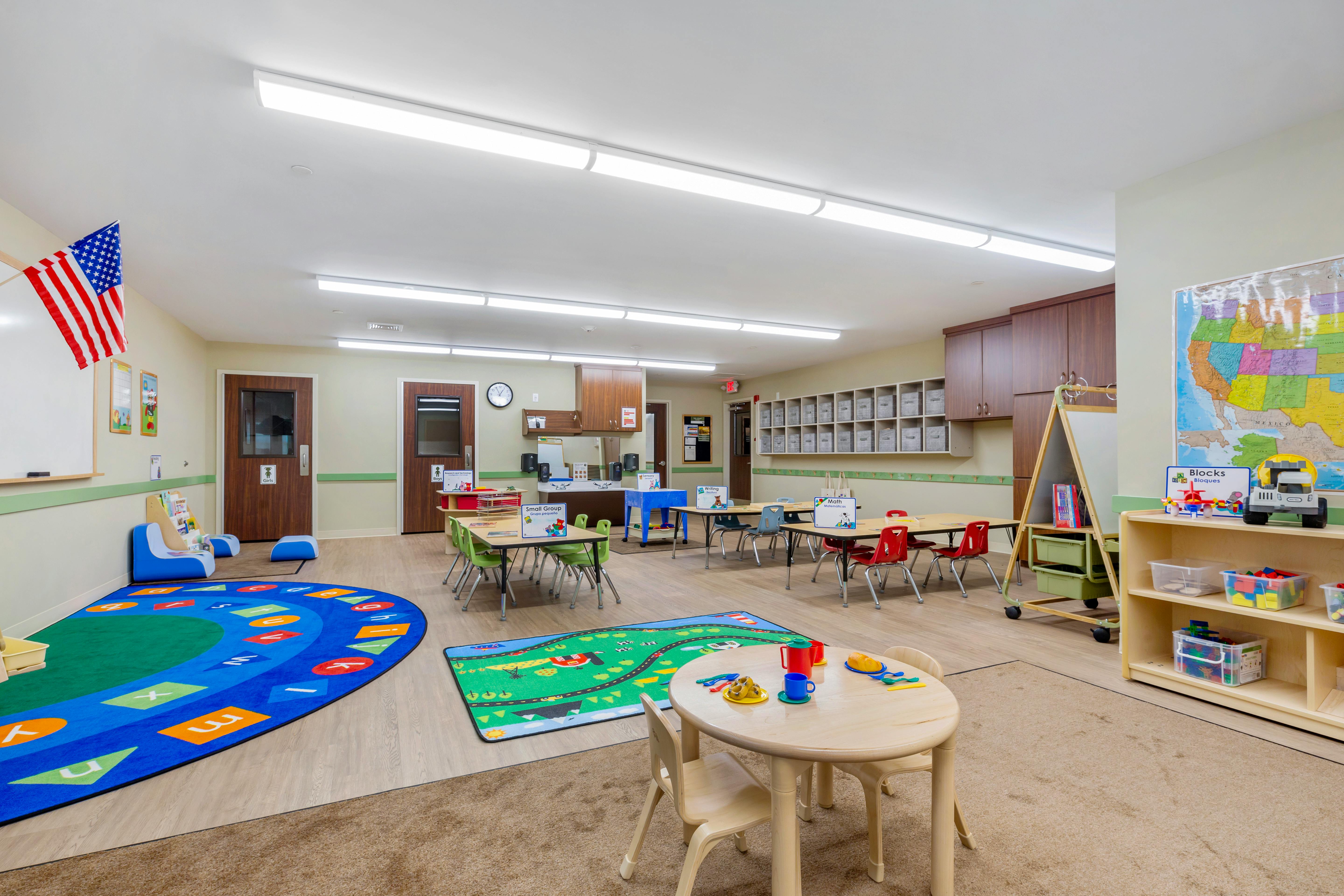 Classroom with multiple child-sized tables and chairs, rugs, and storage cubbies