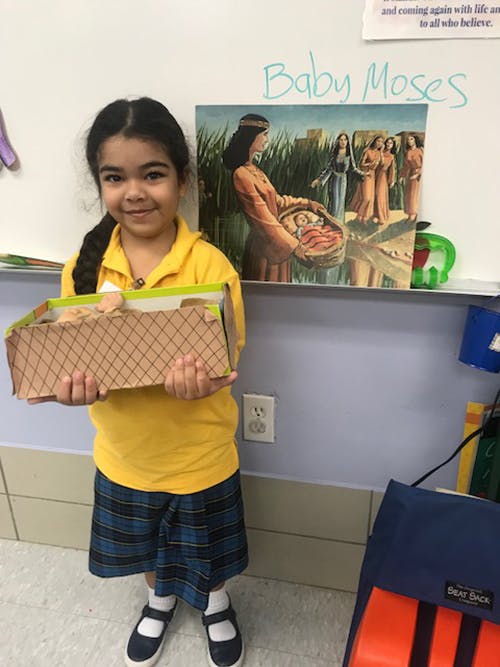 Child holding a box with a painting of Baby Moses in the background