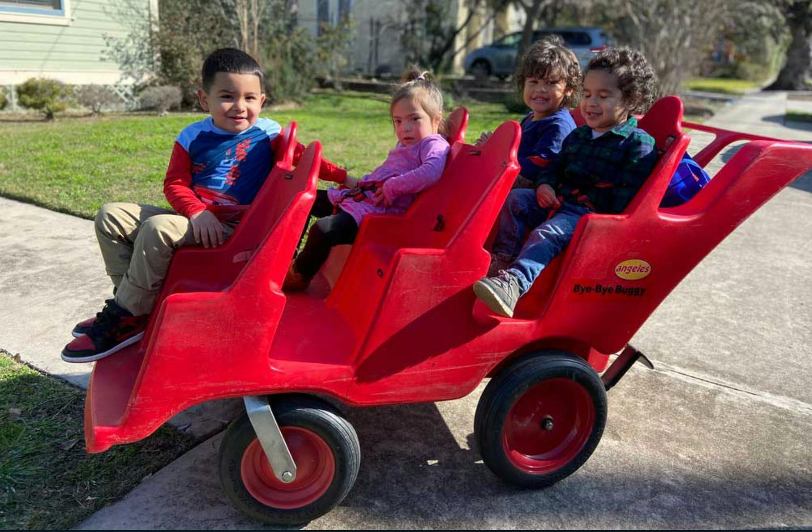 Four children sitting in a red multi-seat wagon