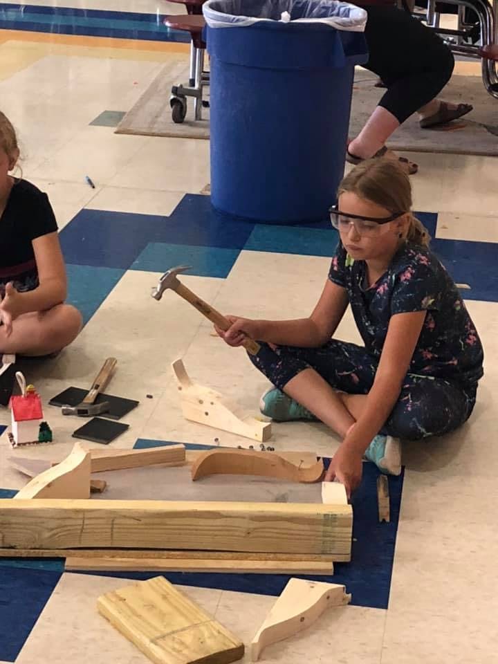 Child wearing safety glasses holding a hammer while sitting on the floor