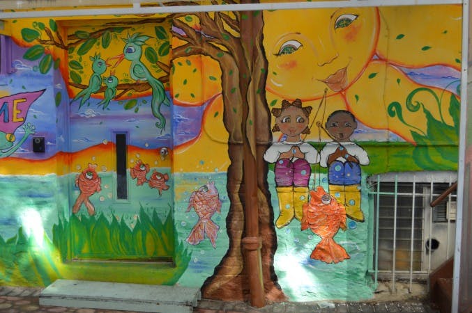 Mural with a tree, sun, birds, fish, and two children