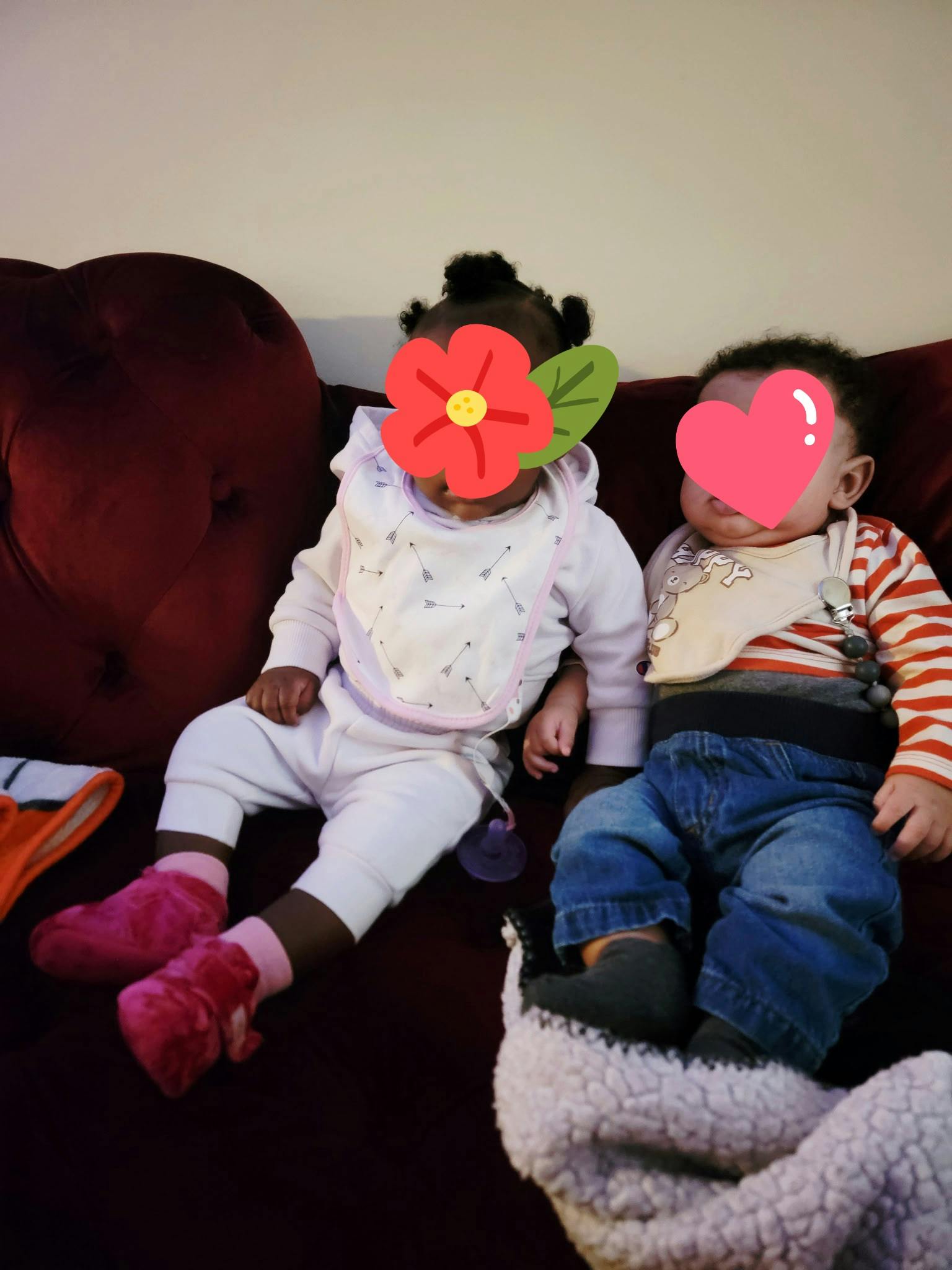Two babies sitting side-by-side on a couch